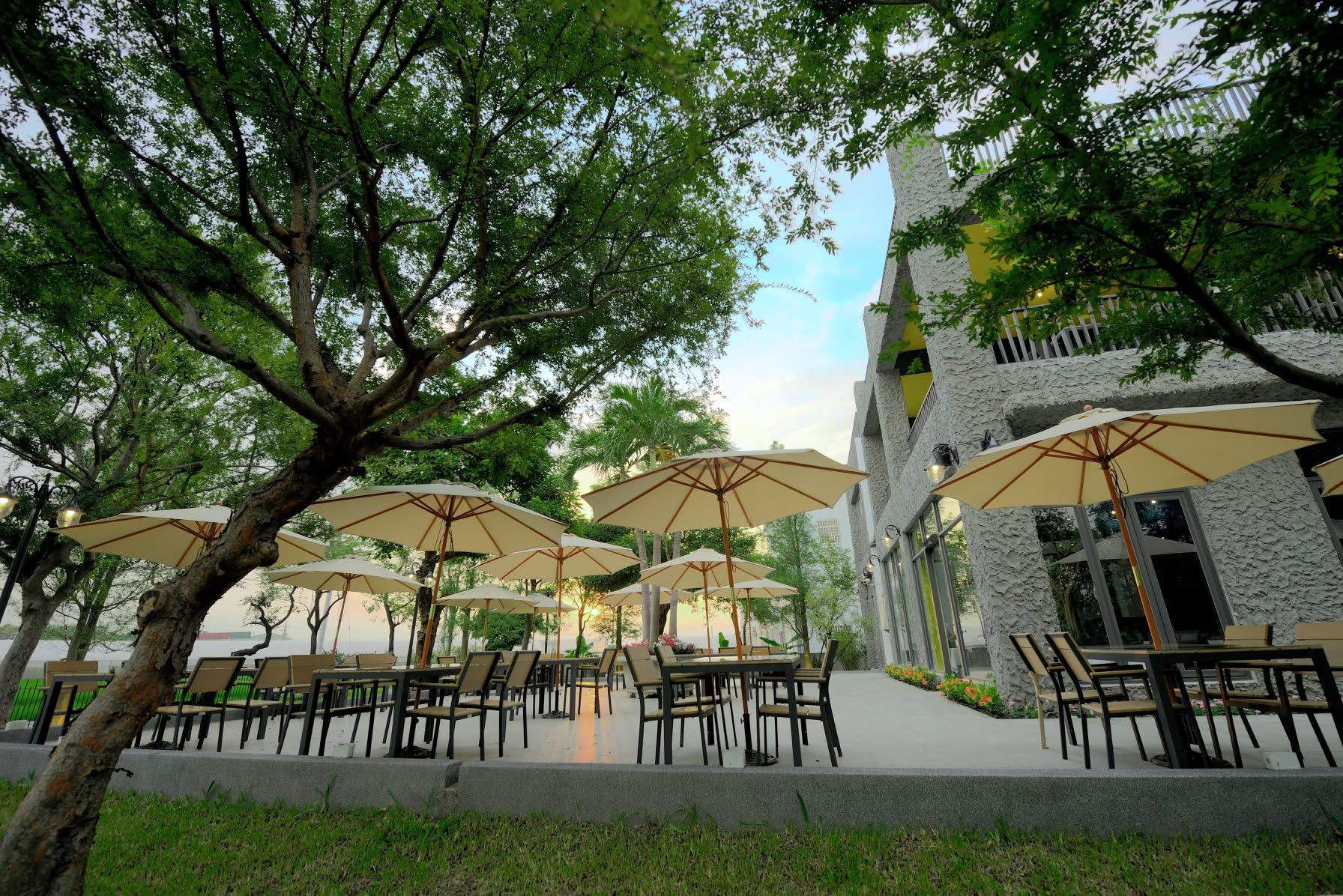 家園戶外用餐區,大樹樹蔭、陽傘與餐桌,旁邊為餐廳建築